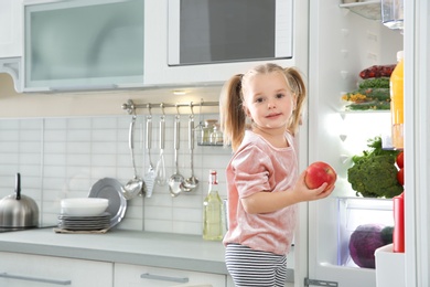 Photo of Cute girl taking apple out of refrigerator in kitchen