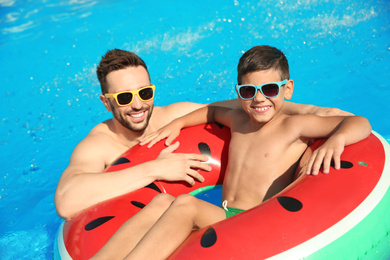 Photo of Father and son with inflatable ring in swimming pool. Family vacation