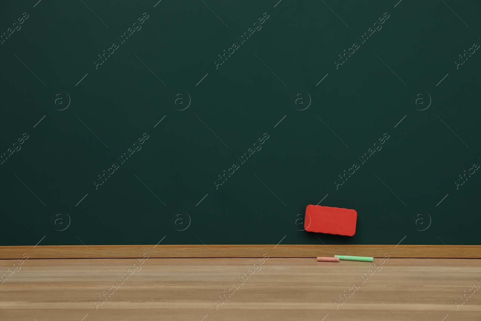 Photo of Colorful chalks on wooden table near green board with duster. Space for text