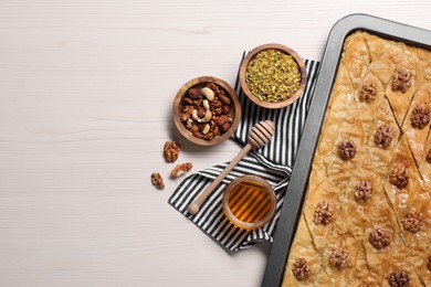 Photo of Delicious baklava with walnuts in baking pan, honey and nuts on white wooden table, flat lay. Space for text