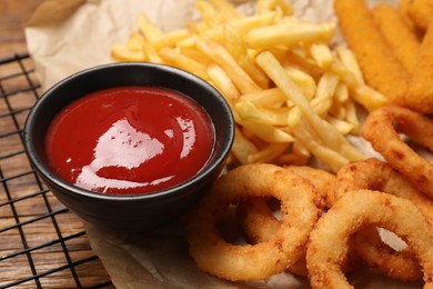 Photo of Tasty ketchup with snacks on wooden table, closeup