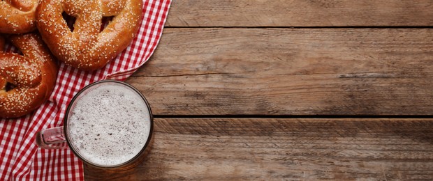 Image of Tasty pretzels and glass of beer on wooden table, flat lay with space for text. Banner design