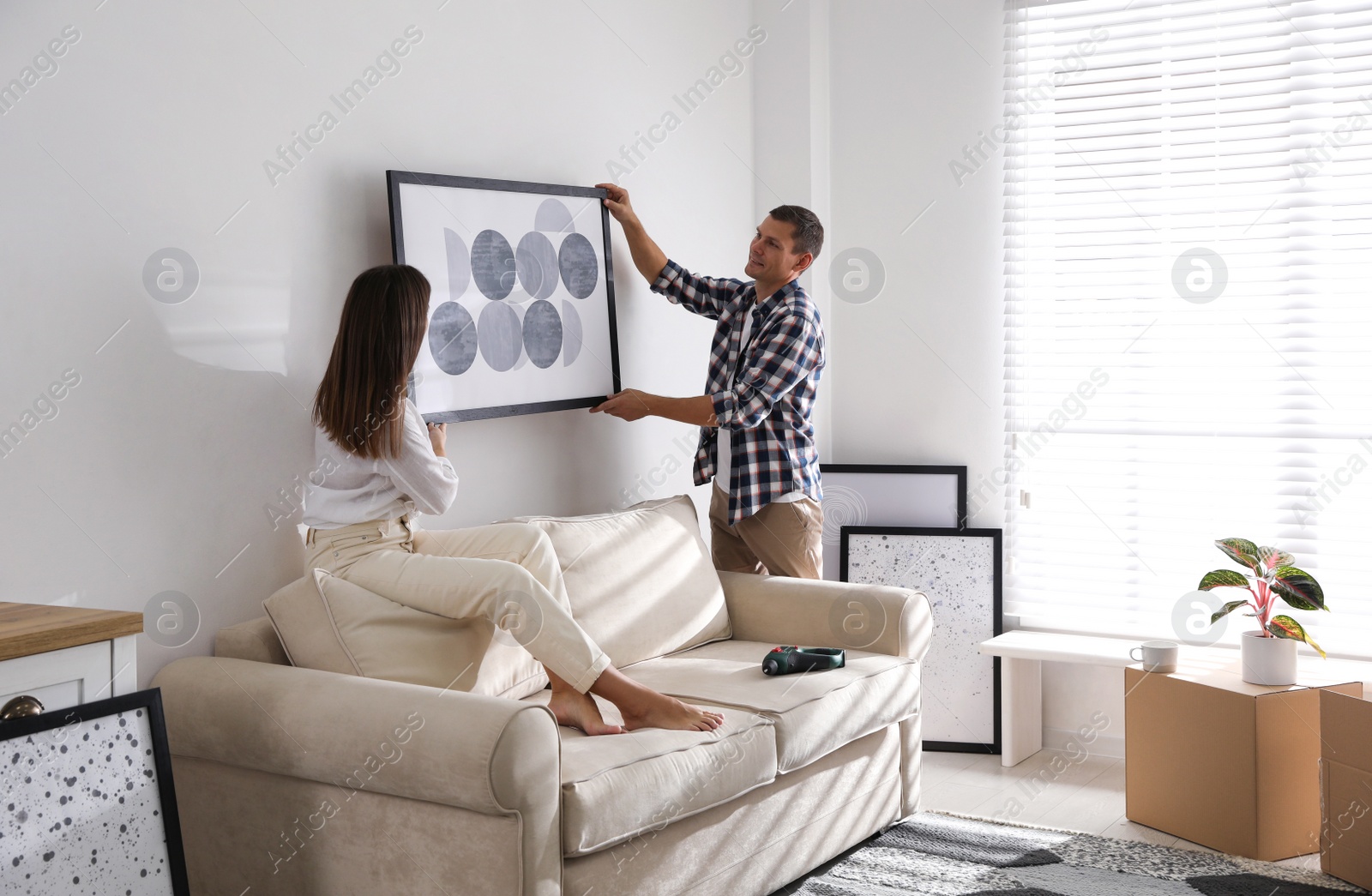 Photo of Happy couple hanging picture on white wall together. Interior design