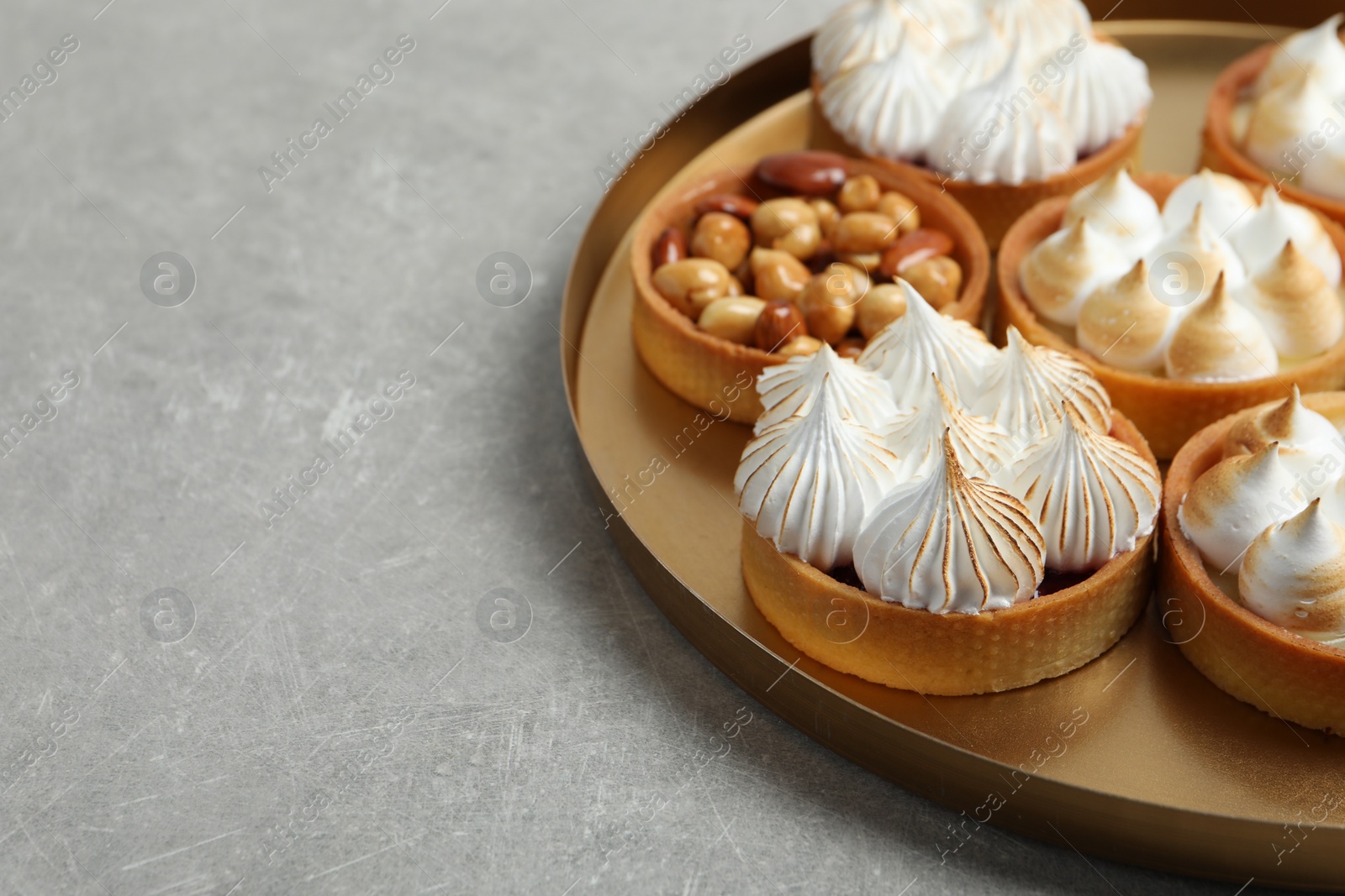 Photo of Many different tartlets on grey table, space for text. Delicious dessert