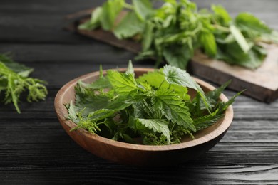 Photo of Fresh stinging nettle leaves in bowl on black wooden table