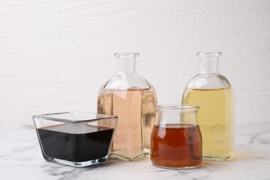 Photo of Different types of vinegar on light marble table, closeup