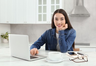 Home workplace. Portrait of happy woman near laptop at marble desk in kitchen