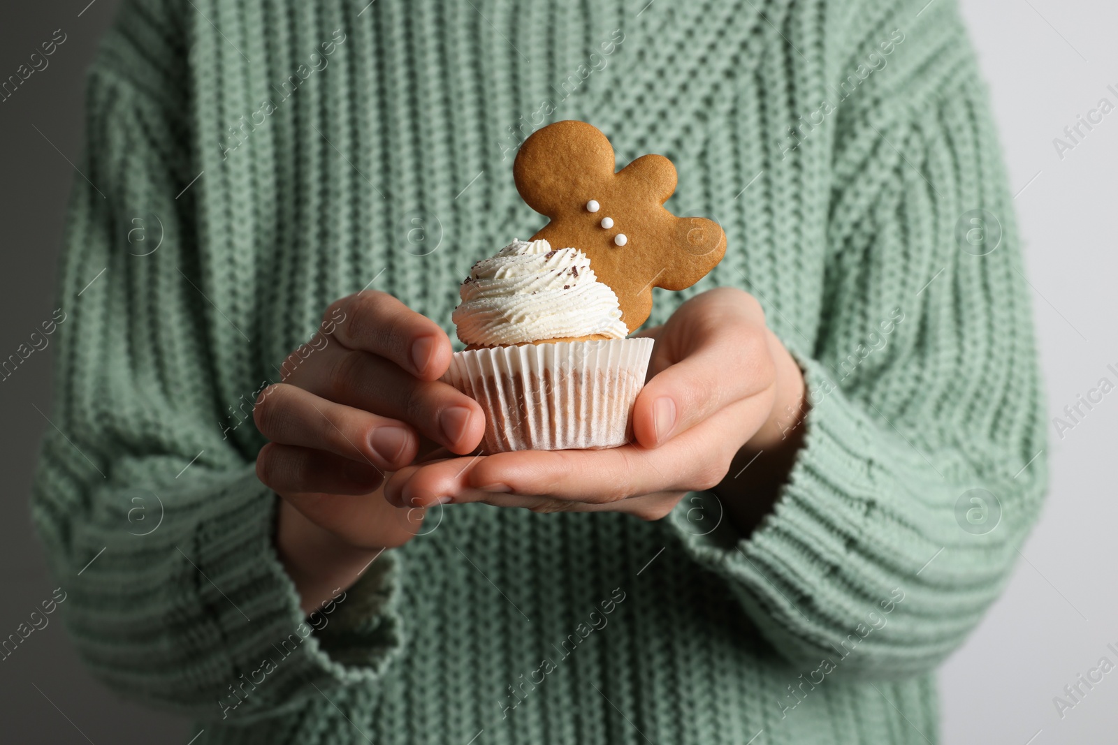 Photo of Woman holding tasty cupcake with gingerbread man cookie on light background, closeup. Christmas celebration