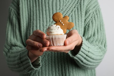 Photo of Woman holding tasty cupcake with gingerbread man cookie on light background, closeup. Christmas celebration