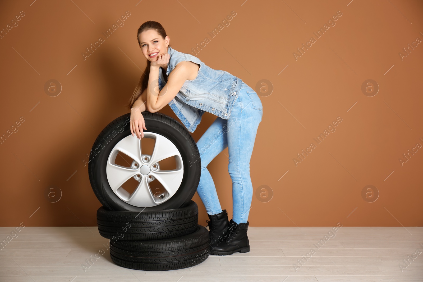 Photo of Young woman in seductive outfit with car tires on color wall background