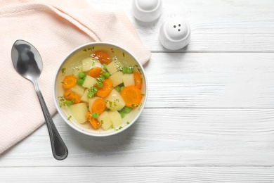 Bowl of fresh homemade vegetable soup served on white wooden table, flat lay. Space for text