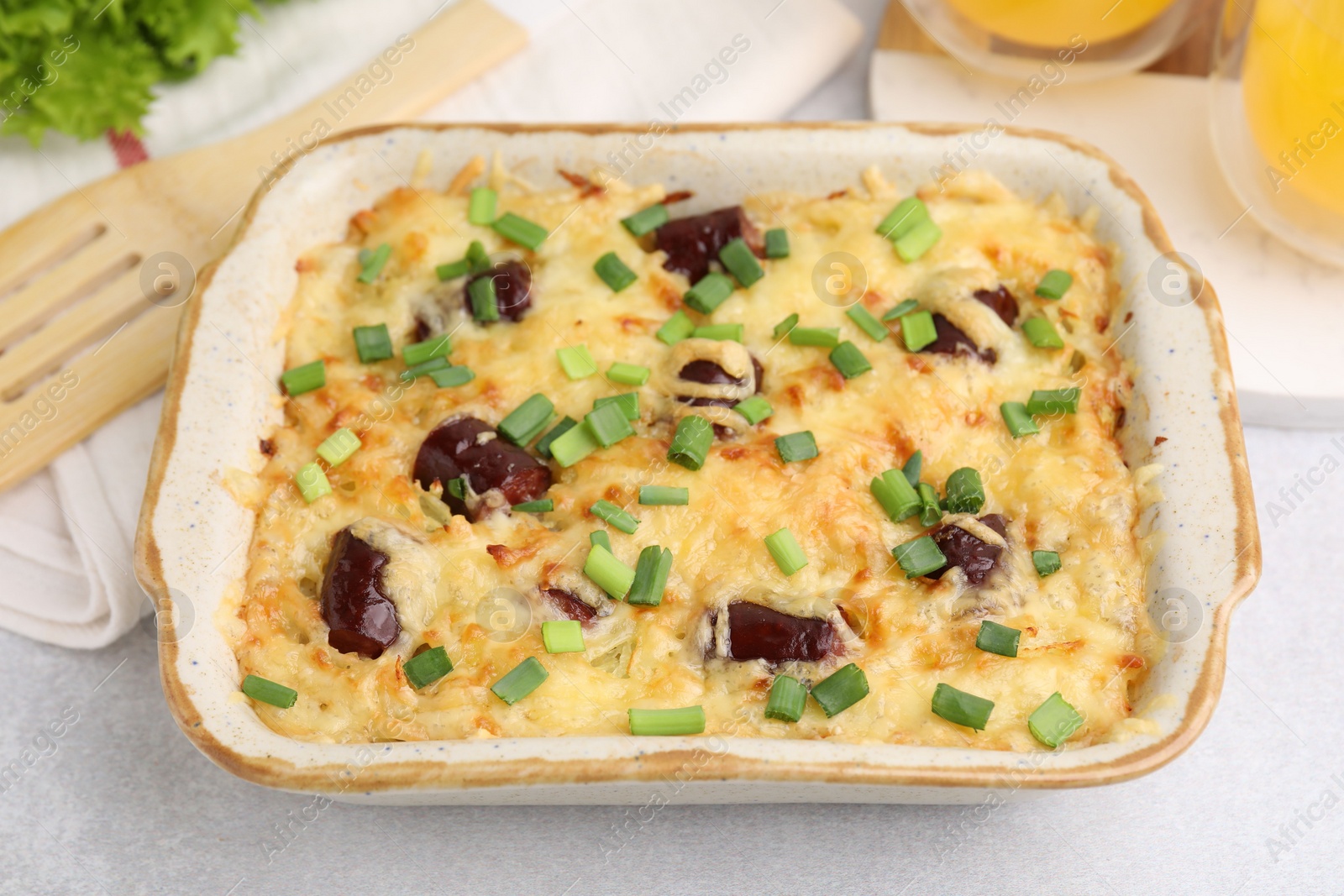 Photo of Tasty sausage casserole with green onions in baking dish on white table, closeup