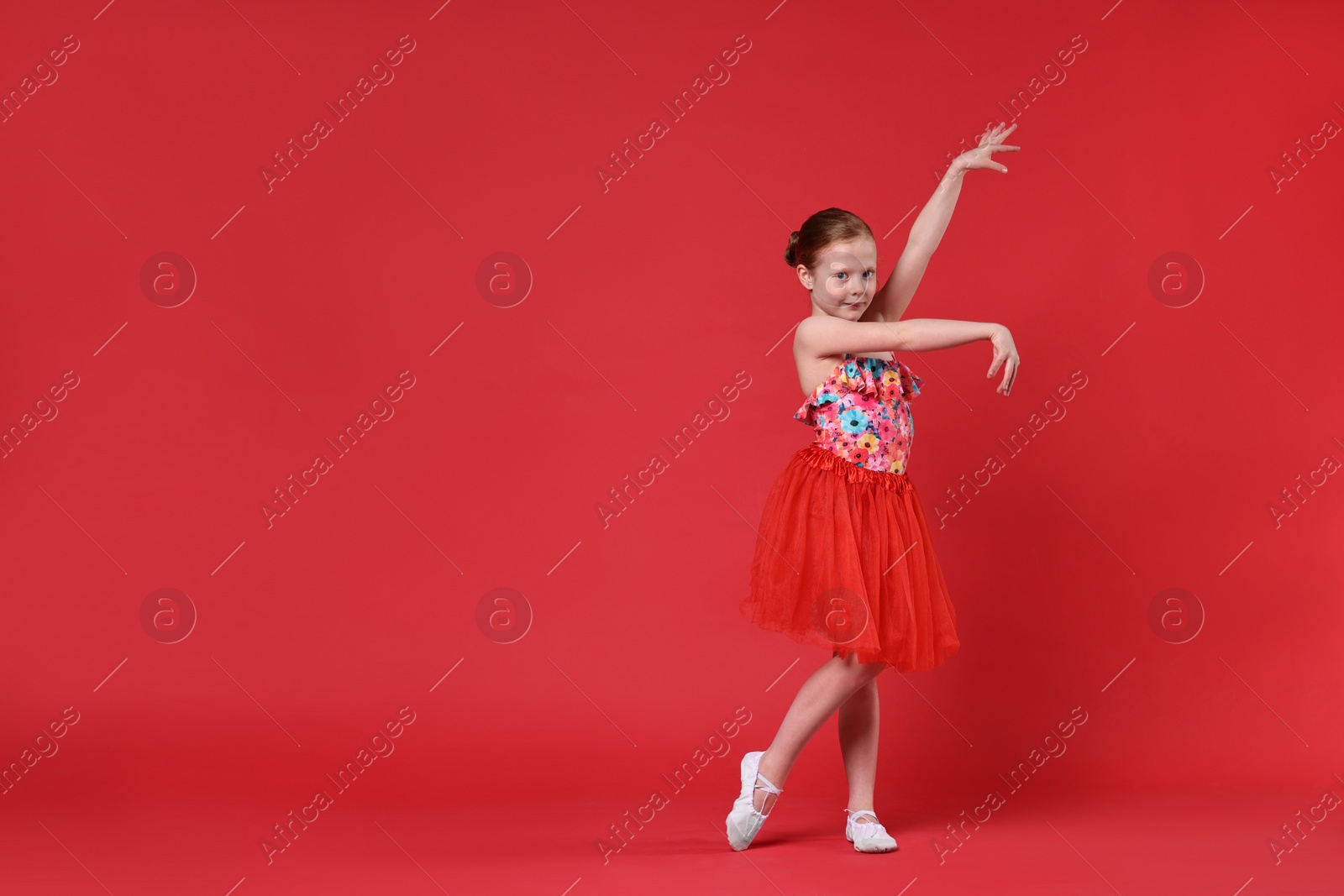 Photo of Cute little girl dancing on red background, space for text