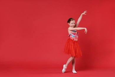 Photo of Cute little girl dancing on red background, space for text