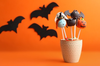 Photo of Delicious Halloween themed cake pops on orange background, space for text
