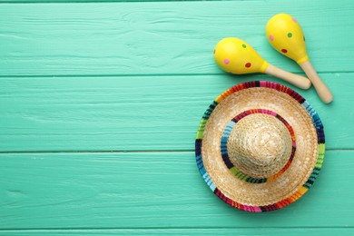 Mexican sombrero hat and maracas on turquoise wooden table, flat lay. Space for text