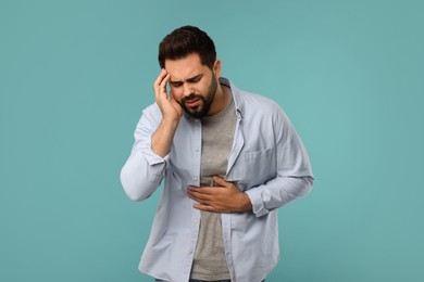 Young man suffering from stomach pain on light blue background