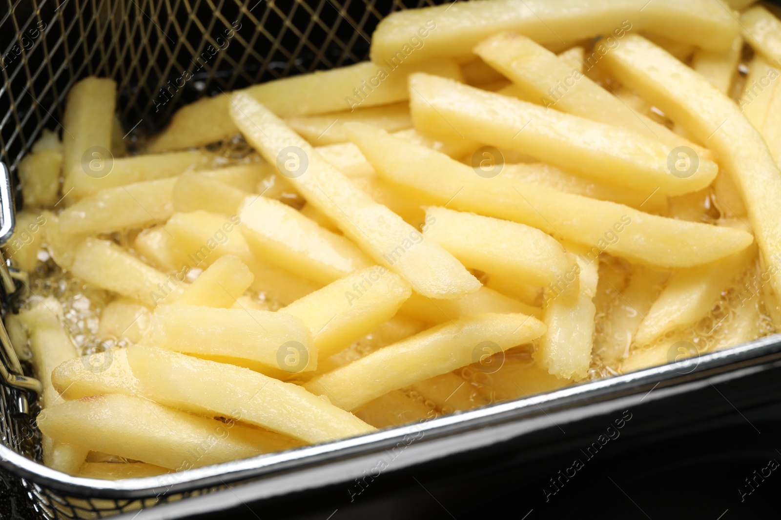 Photo of Cooking delicious french fries in hot oil, closeup