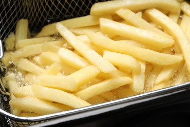 Cooking delicious french fries in hot oil, closeup