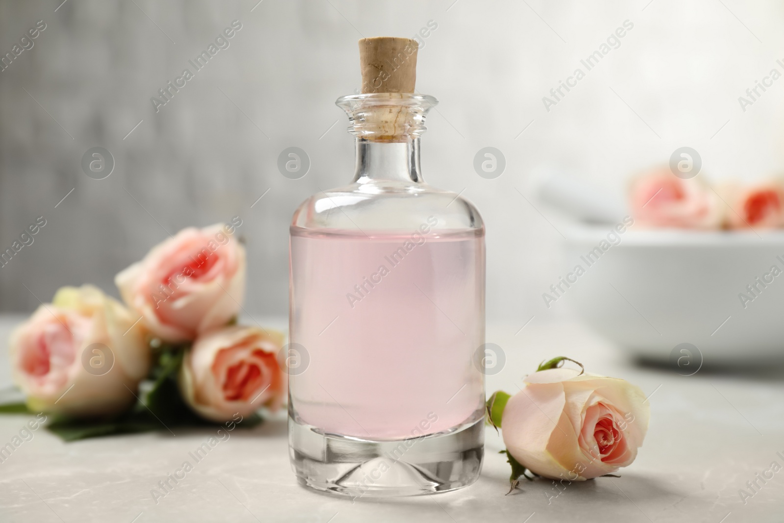 Photo of Bottle of rose essential oil and flowers on white table