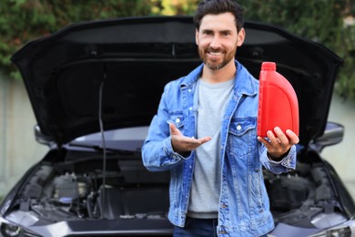 Photo of Smiling man showing motor oil near car outdoors, focus on red container