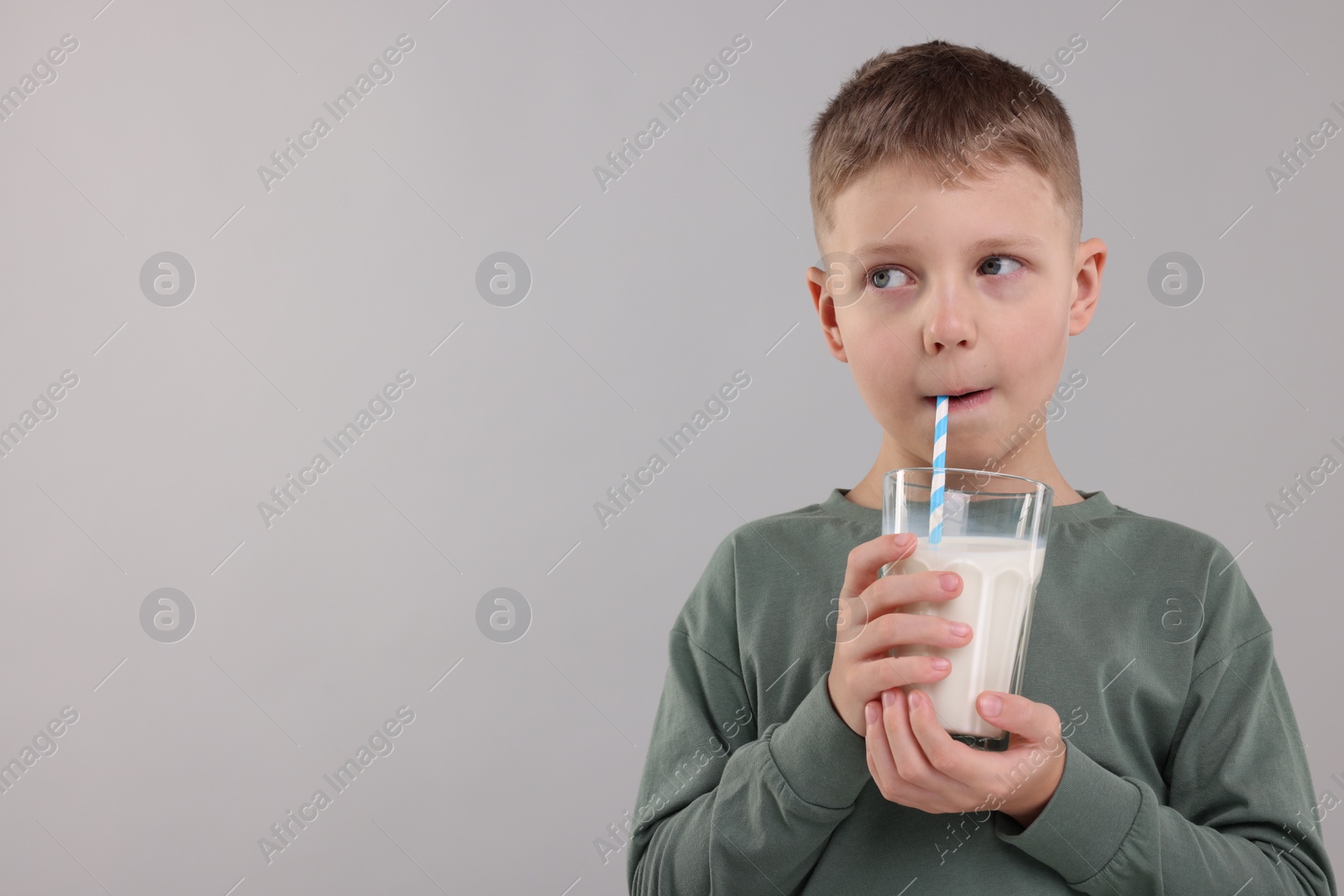 Photo of Cute boy drinking fresh milk from glass on light grey background, space for text
