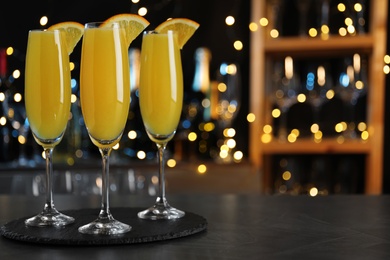 Mimosa cocktail with garnish on bar counter against blurred lights, space for text