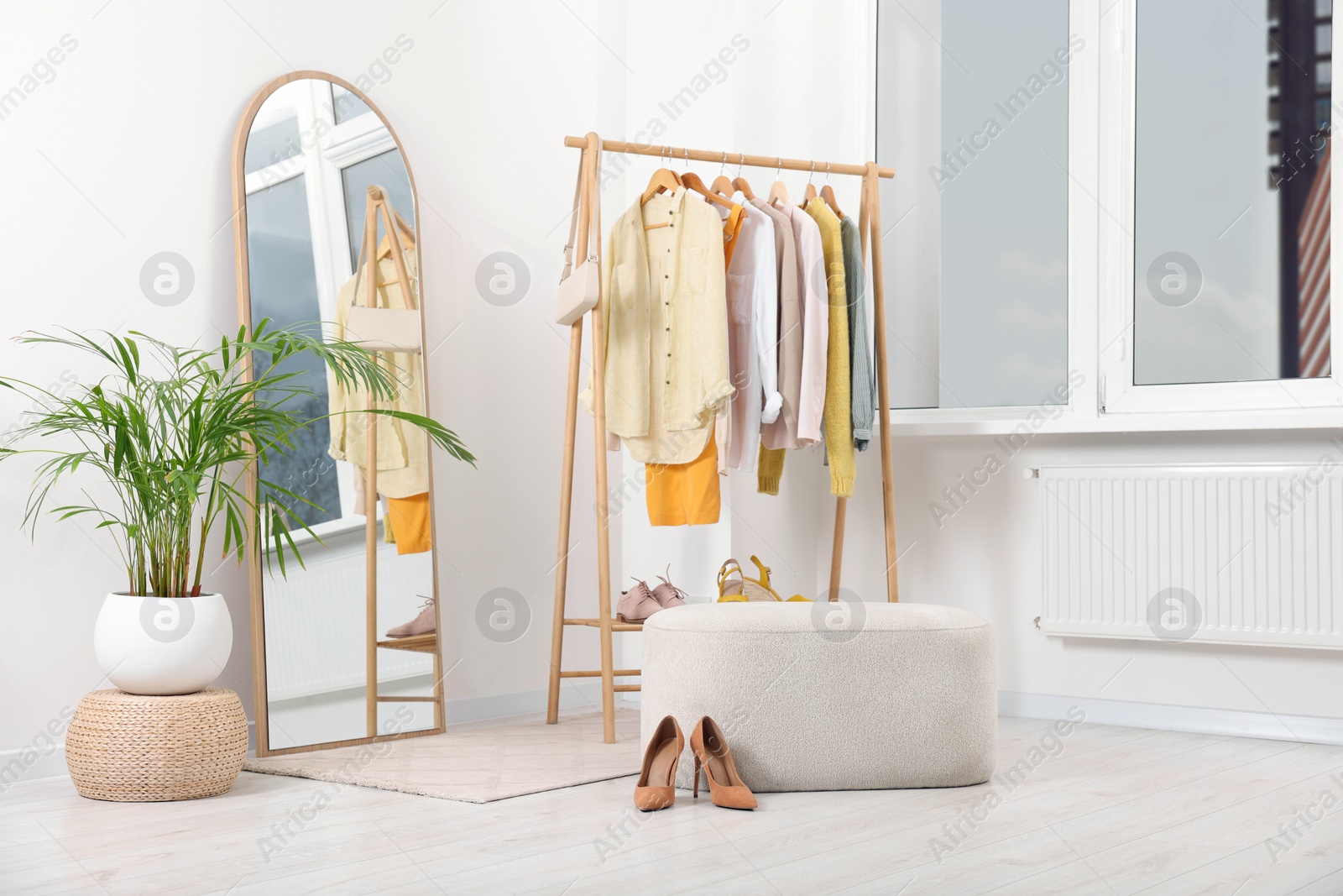 Photo of Stylish dressing room interior with mirror, ottoman and clothing rack