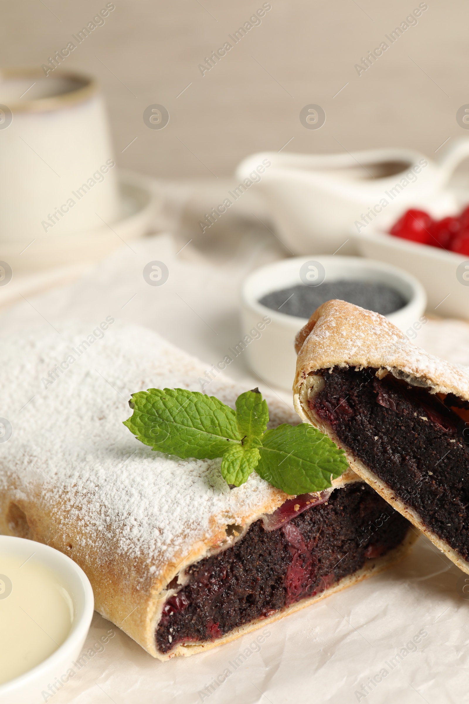 Photo of Delicious strudel with cherries and poppy seeds on parchment, closeup