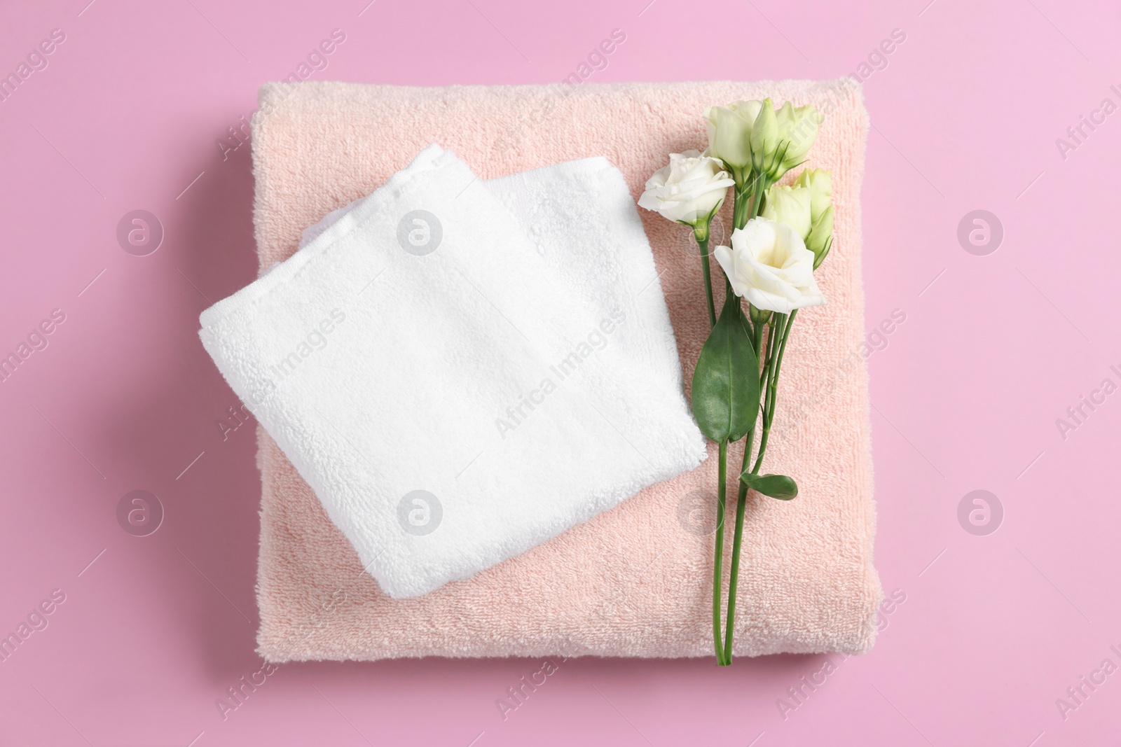 Photo of Soft folded towels with flowers on violet background, top view