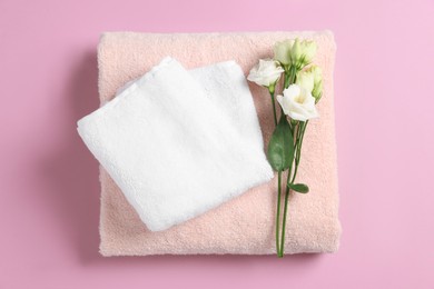 Soft folded towels with flowers on violet background, top view