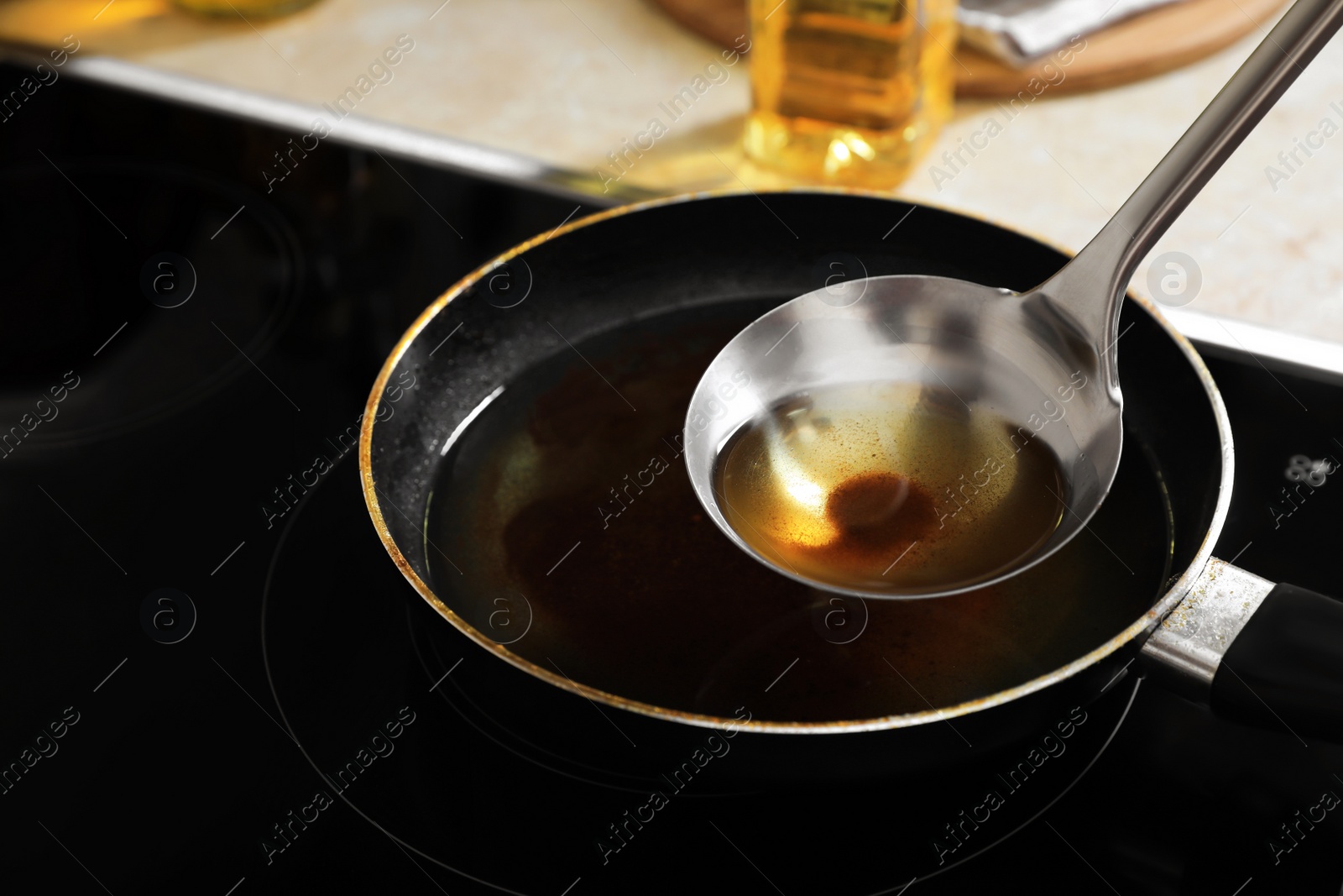 Photo of Ladle with used cooking oil over frying pan on stove