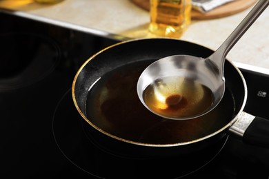 Ladle with used cooking oil over frying pan on stove