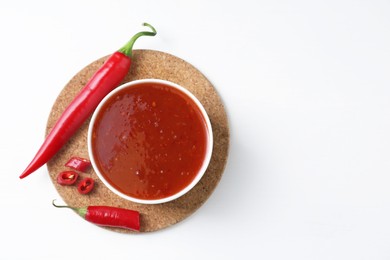 Photo of Spicy chili sauce in bowl and fresh peppers on white background, top view. Space for text