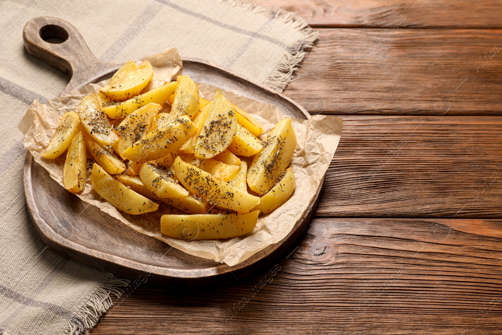 Photo of Board with tasty baked potato wedges and spices on wooden table, space for text