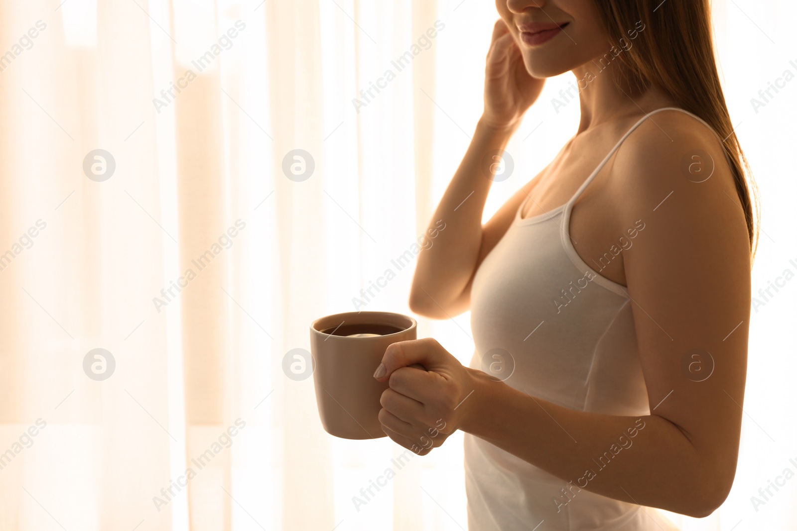 Photo of Young woman with cup near window at home, closeup. Lazy morning