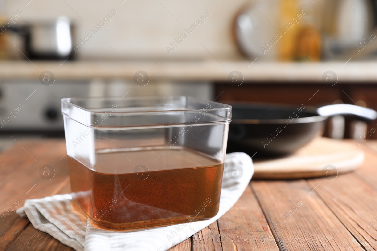 Photo of Container with used cooking oil on wooden table in kitchen