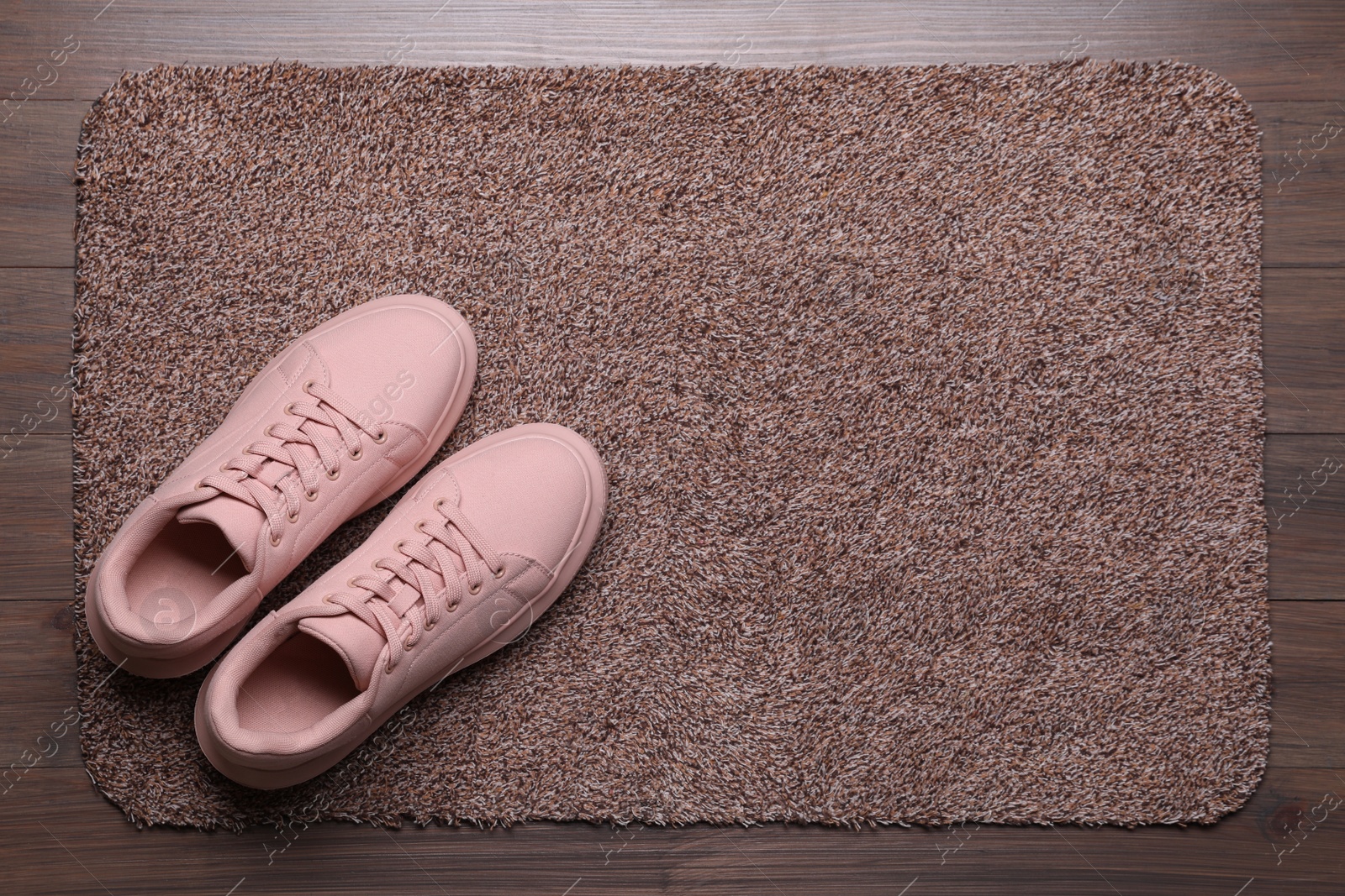 Photo of New clean door mat with shoes on wooden floor, above view