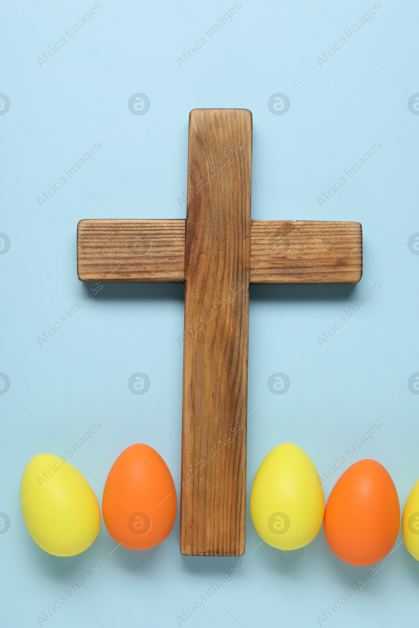 Photo of Wooden cross and painted Easter eggs on light blue background, flat lay