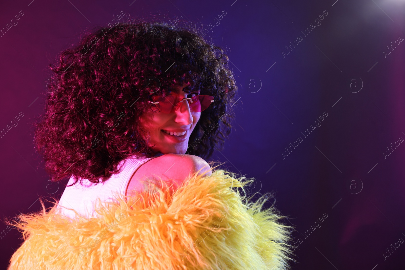 Photo of Beautiful young woman in yellow fur coat and sunglasses on color background in neon lights