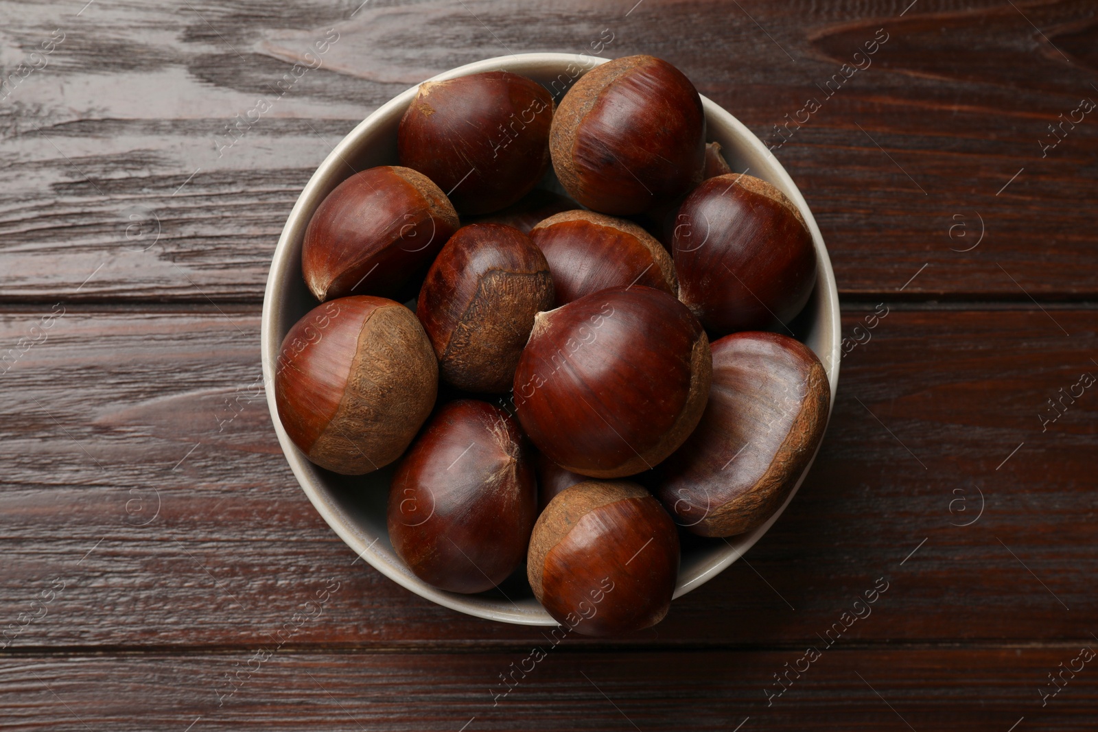 Photo of Sweet fresh edible chestnuts in bowl on wooden table, top view