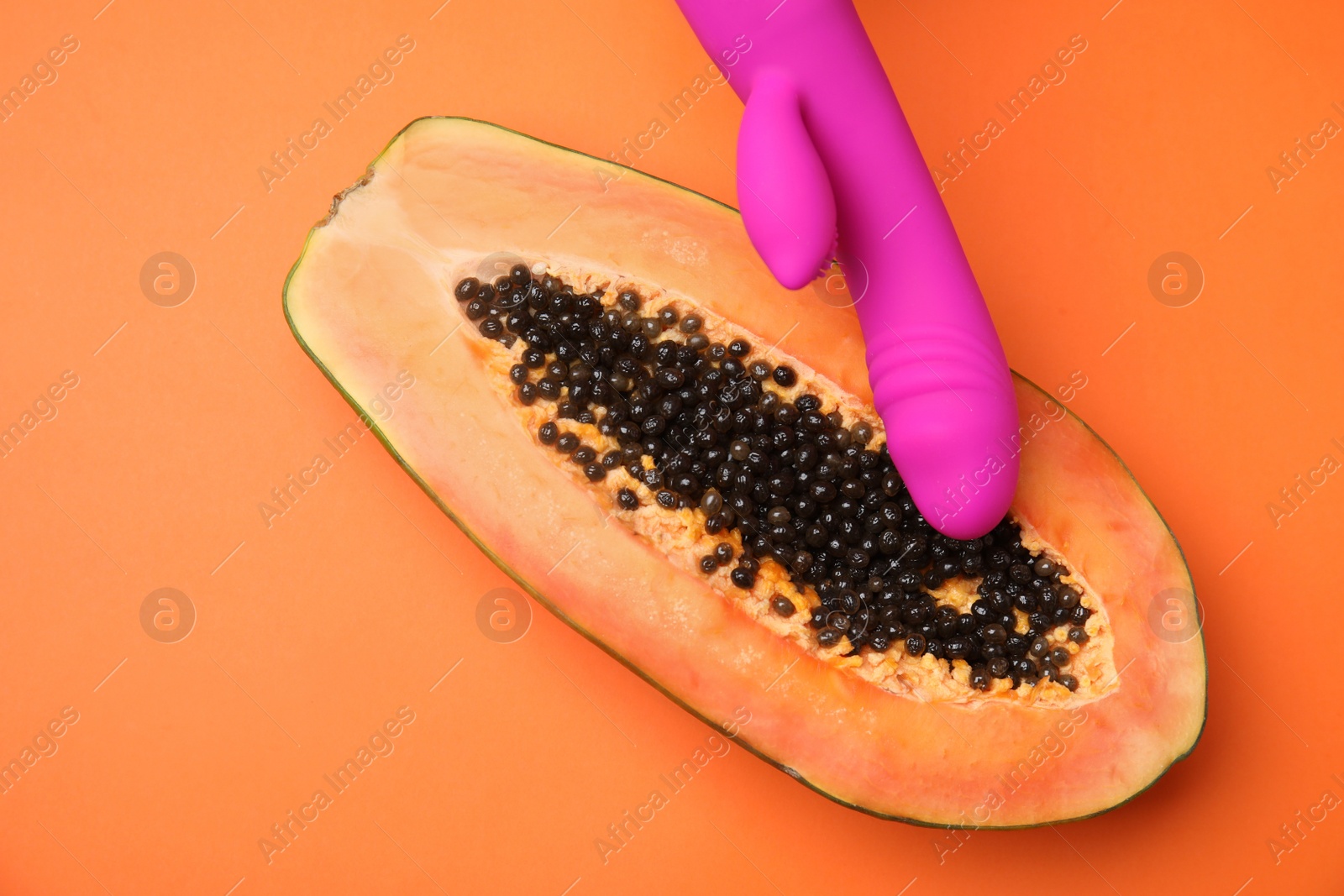 Photo of Half of papaya and purple vibrator on orange background, top view. Sex concept