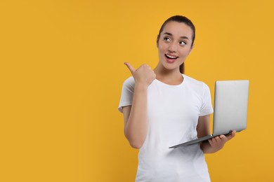 Photo of Special promotion. Smiling woman with laptop pointing at something on orange background. Space for text