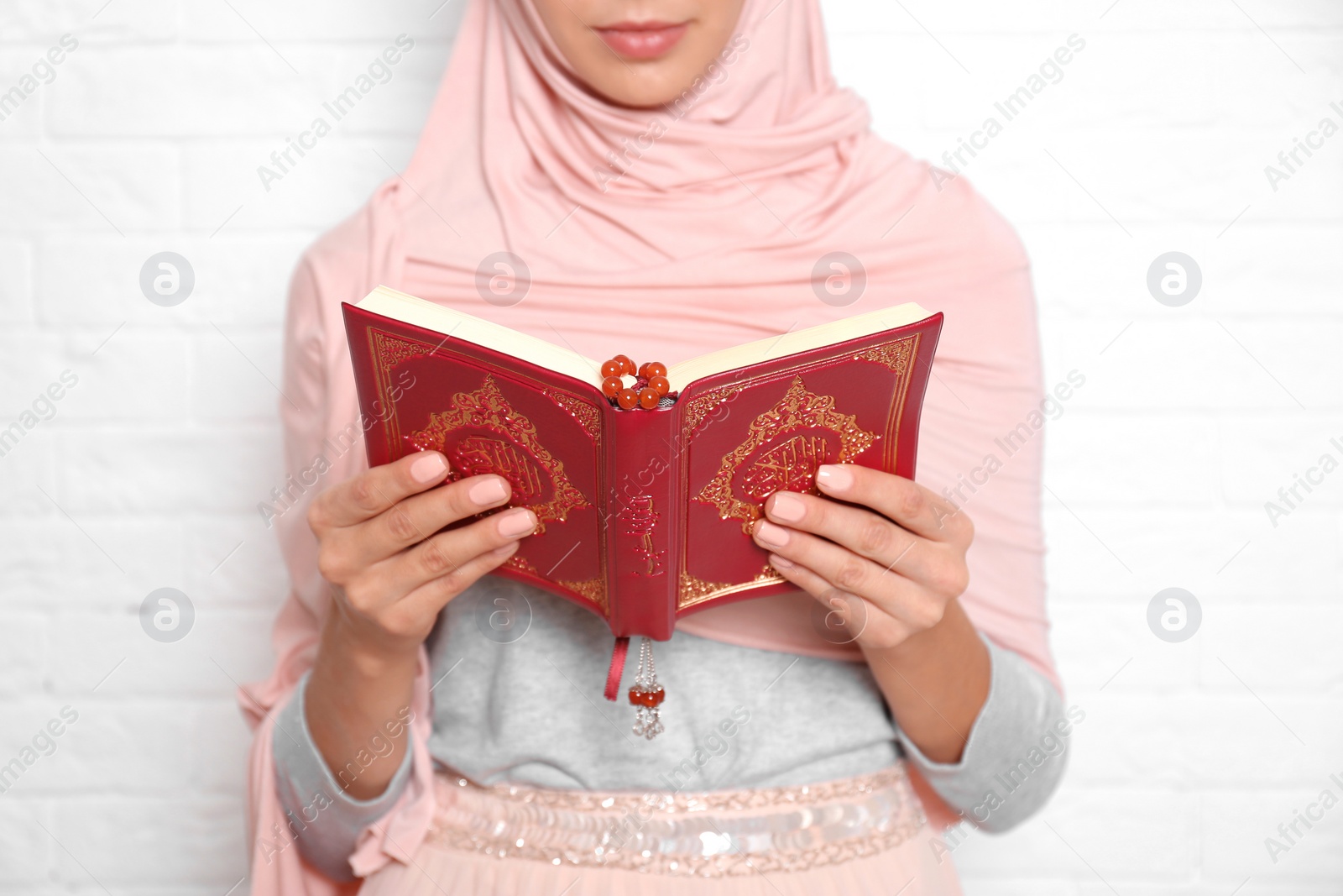 Photo of Young Muslim woman reading Koran against brick wall, closeup