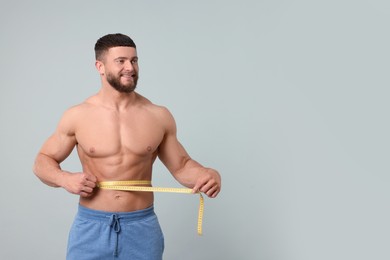 Photo of Portrait of happy athletic man measuring waist with tape on light grey background, space for text. Weight loss concept