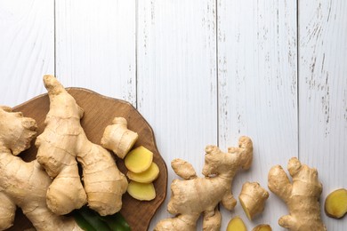 Photo of Cut and whole fresh ginger with leaves on white wooden table, flat lay. Space for text