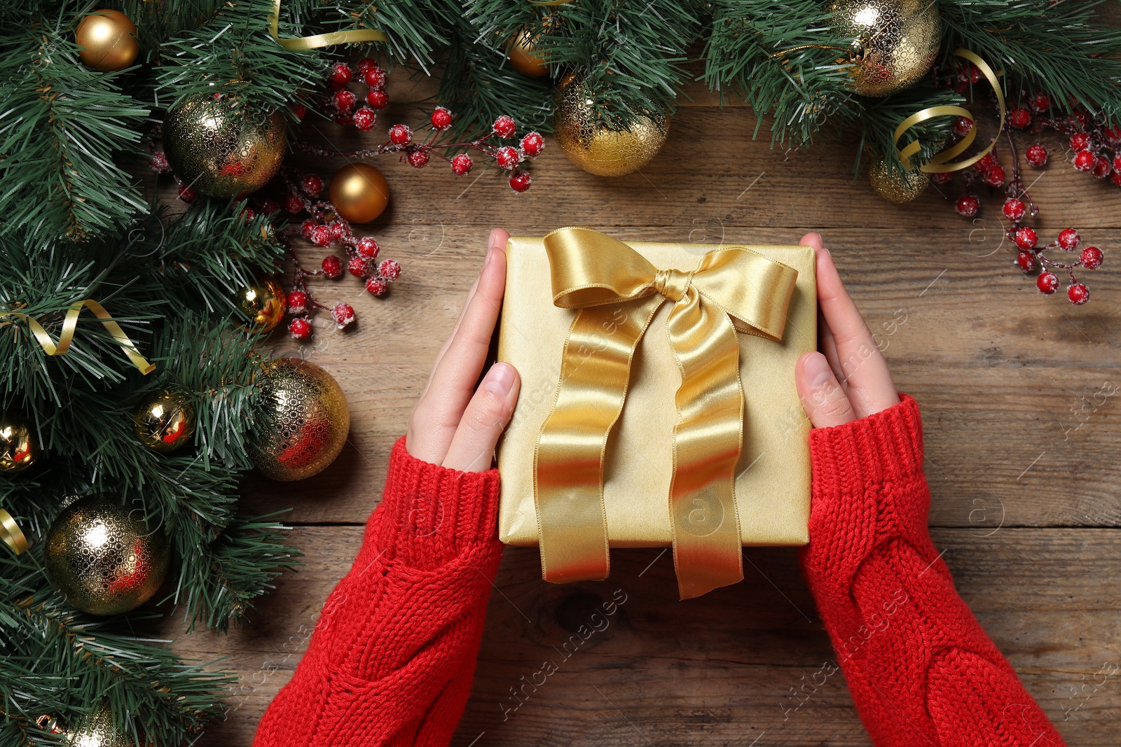 Photo of Christmas present. Woman with gift box and decorated fir tree branches at wooden table, top view