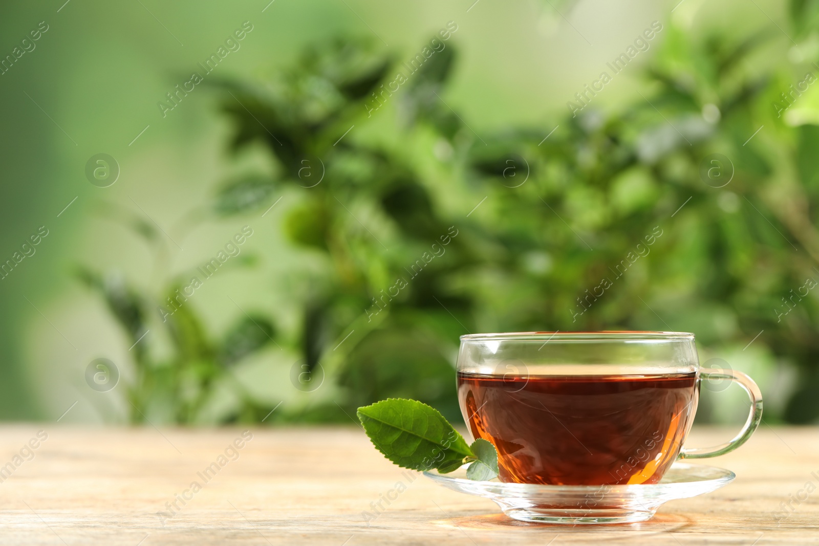 Photo of Cup of black tea on wooden table against blurred background. Space for text