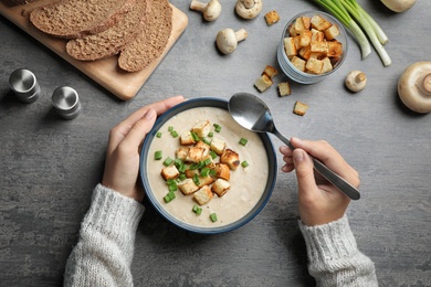 Woman eating fresh homemade mushroom soup from bowl on table, top view