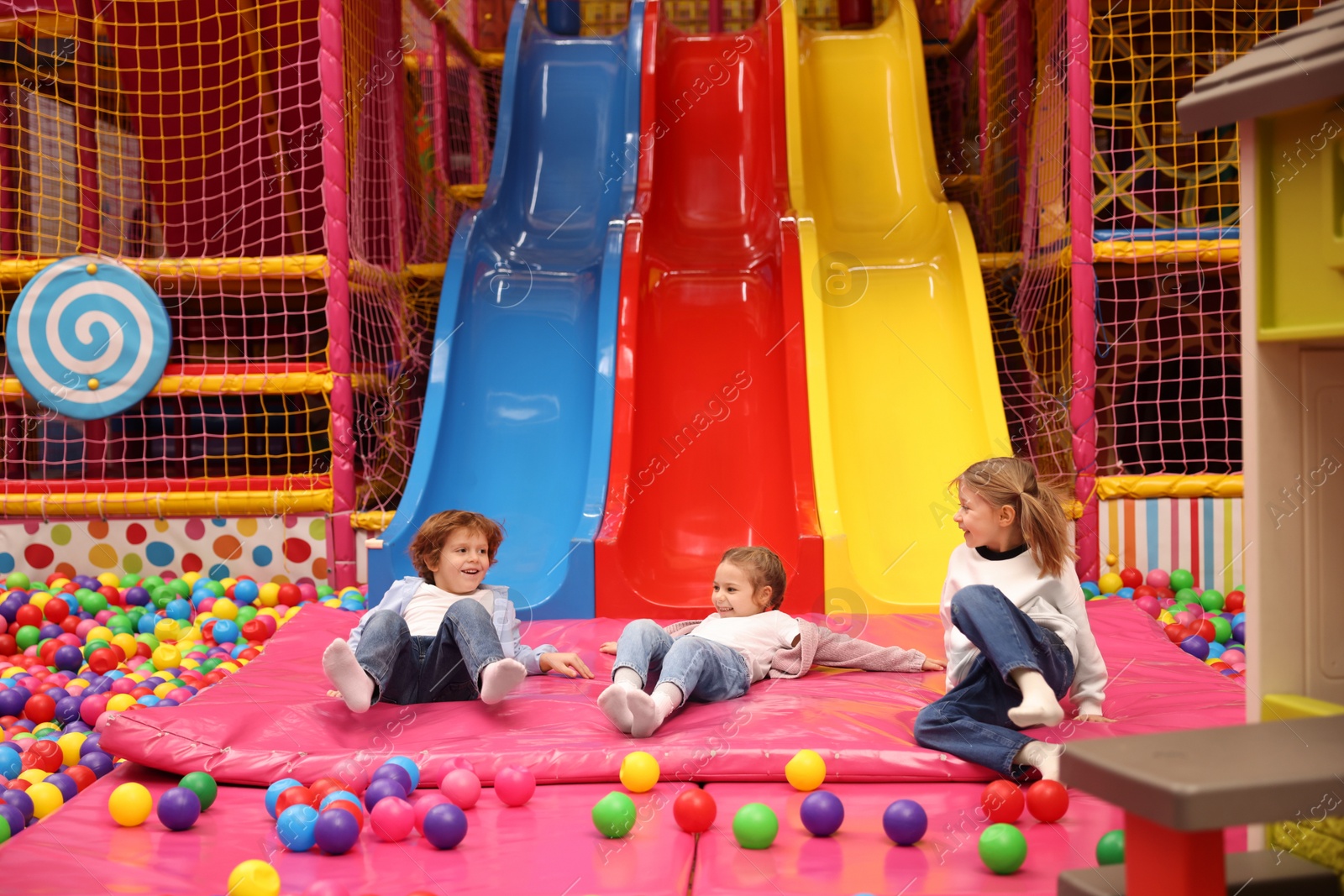 Photo of Happy kids playing in play room with slides, mats and ball pit